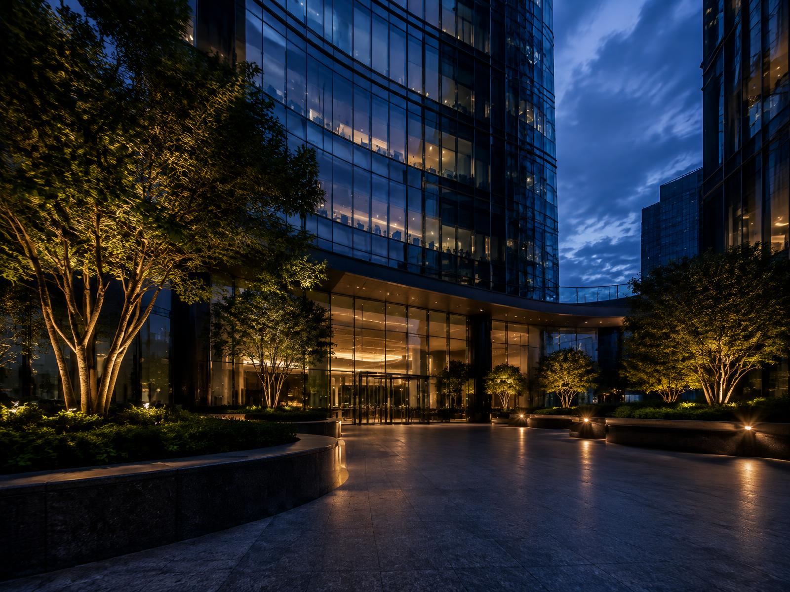 Generic modern glass office tower courtyard entrance with uplit trees at dusk