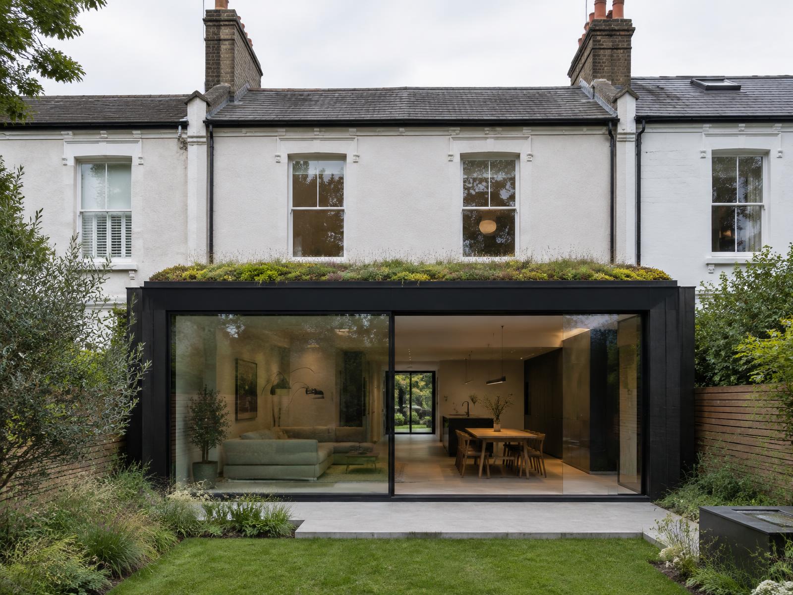 White Victorian terrace with a blackened steel and glass garden extension topped by a green roof