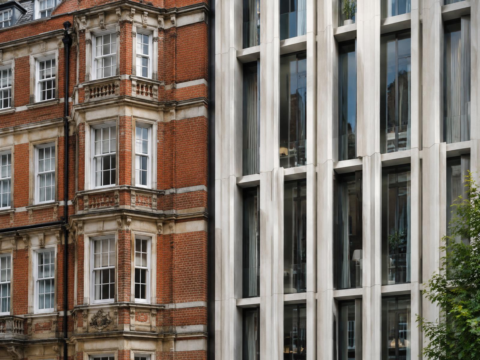 Red-brick Edwardian mansion block directly beside a contemporary building with pale vertical fins and deep glazing