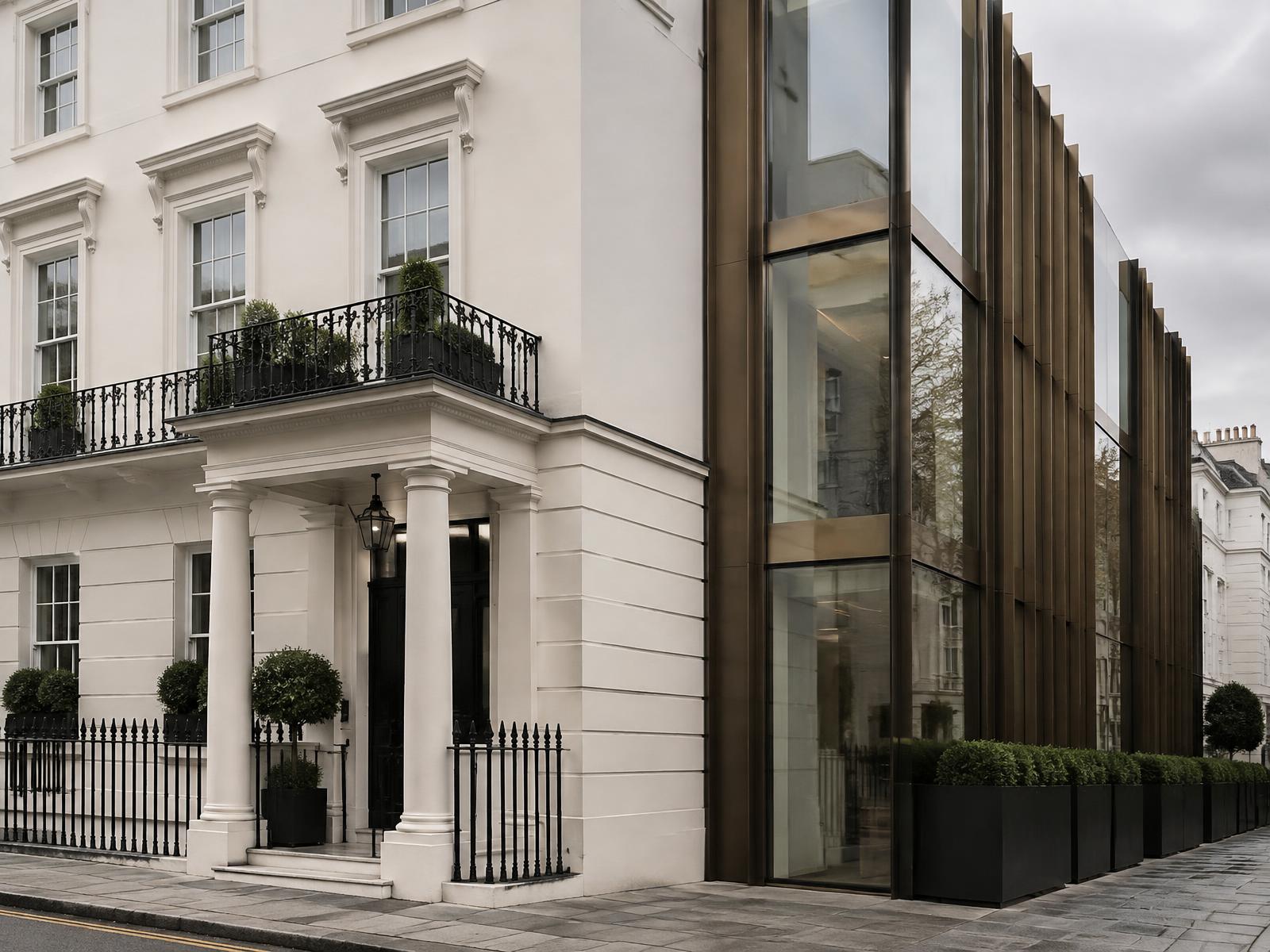 Cream stucco Belgravia terrace house with portico directly beside a contemporary bronze-finned glass building