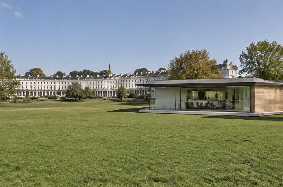 Contemporary glass pavilion house on the open heath with a Georgian crescent beyond in Blackheath