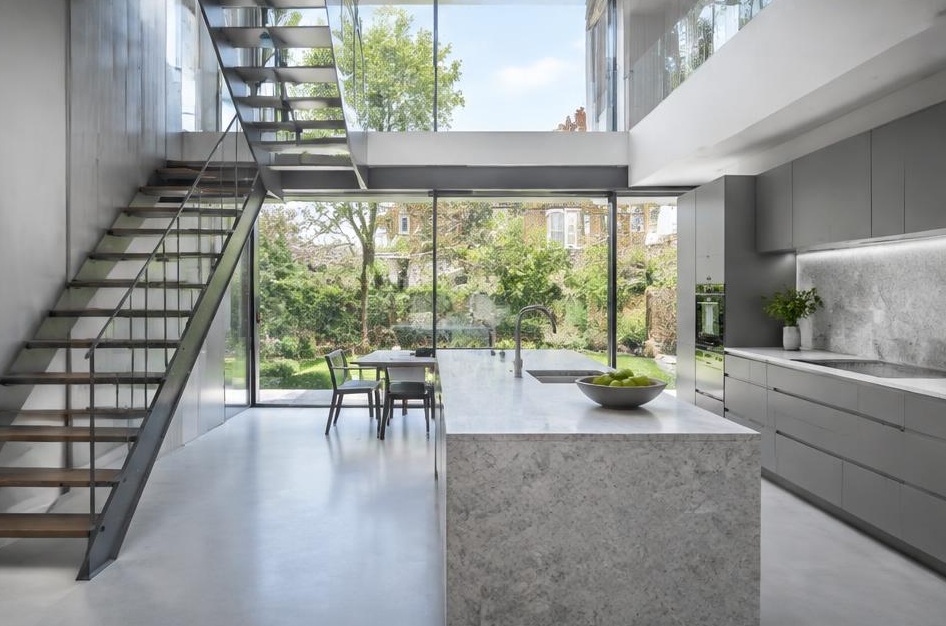 Contemporary kitchen with open staircase and glazing onto a residential garden in Brackenbury Village