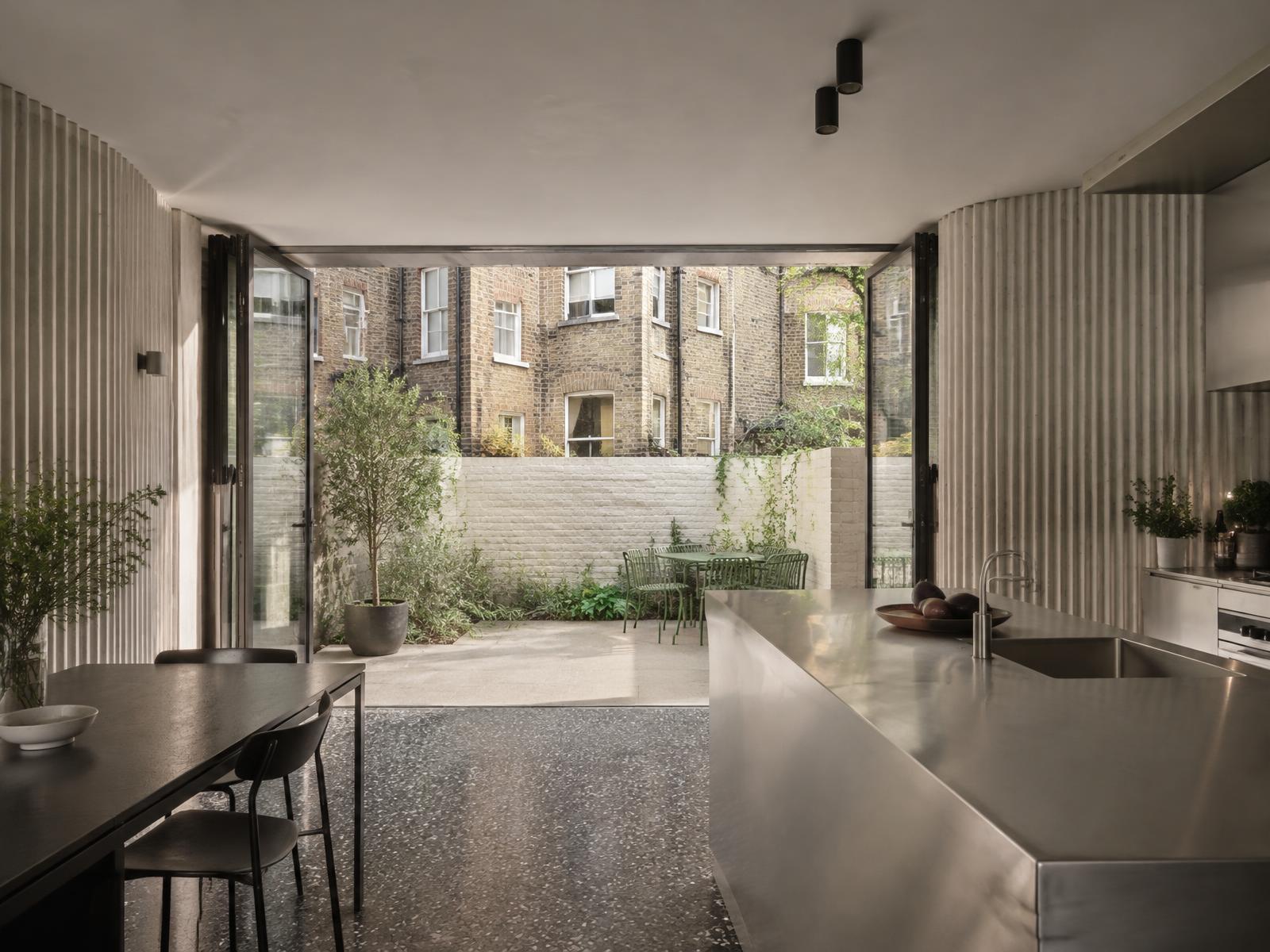 New garden-level kitchen with fluted concrete walls opening onto a brick-walled courtyard