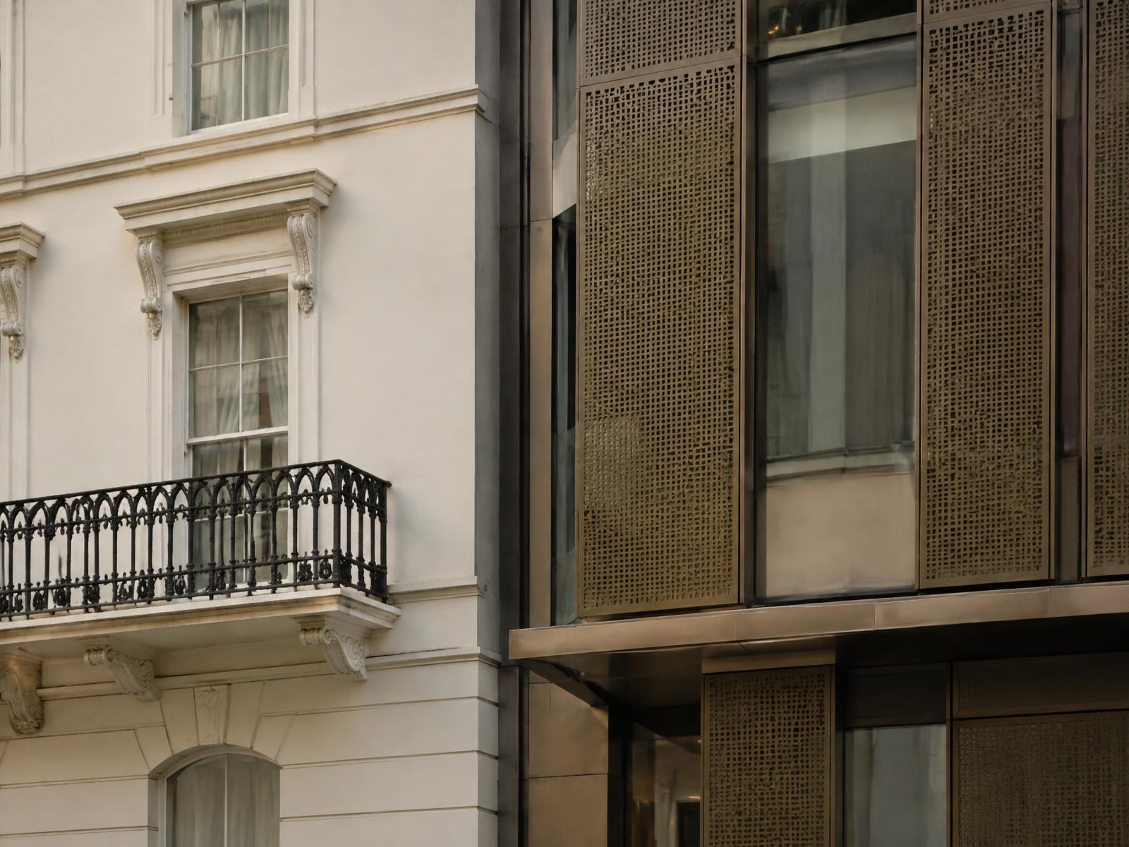 Listed stucco terrace with iron balcony directly beside perforated bronze screens and glass