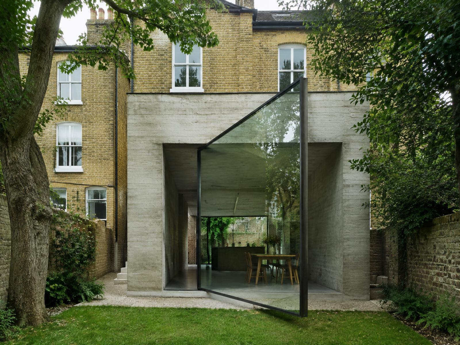 Board-marked concrete rear extension with a huge pivoting glass door behind a yellow-brick Victorian townhouse