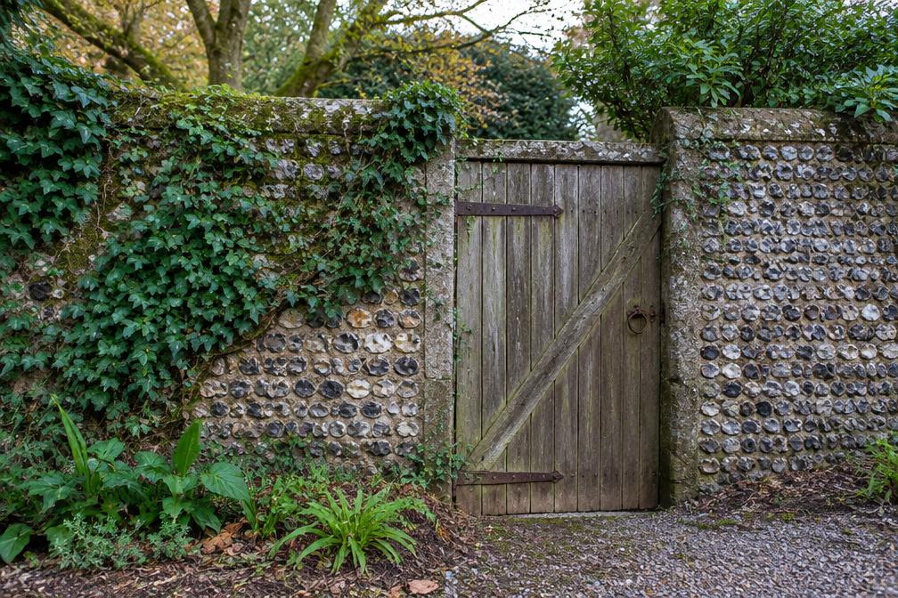 Historic flint garden wall with a weathered timber gate and climbing ivy
