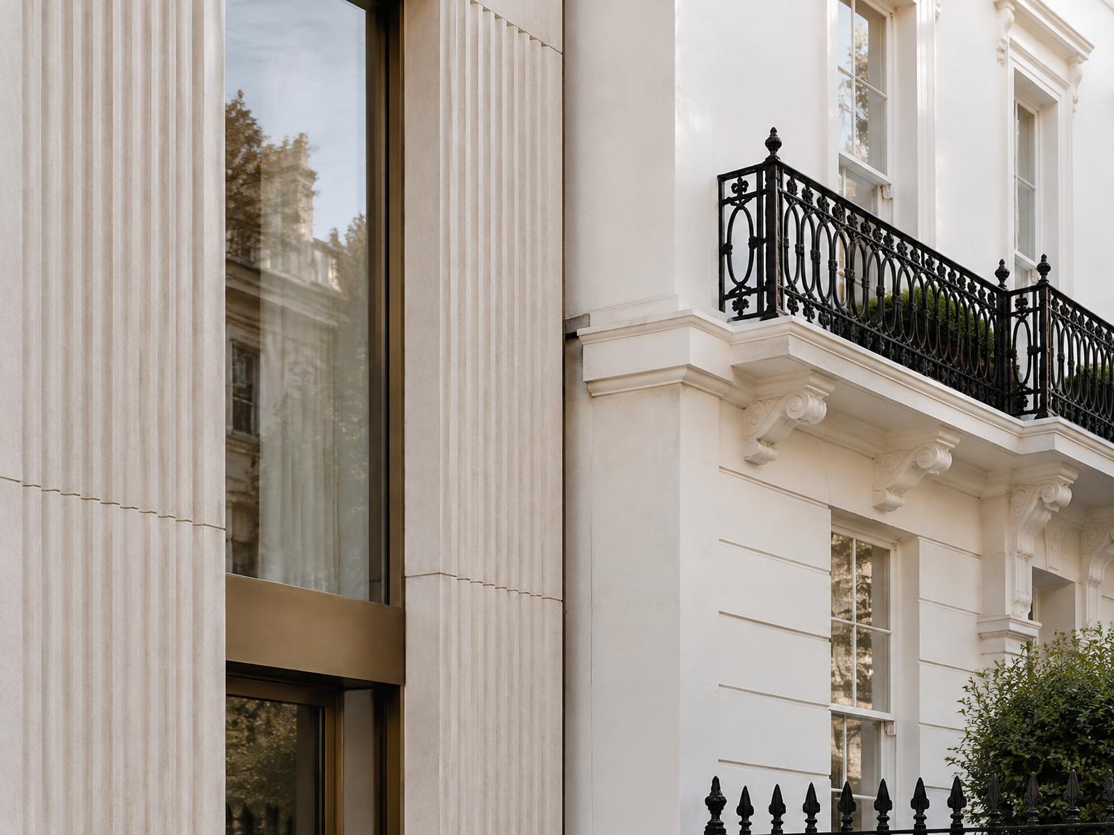 Contemporary fluted-stone facade meeting a listed white stucco Chelsea terrace with iron balcony