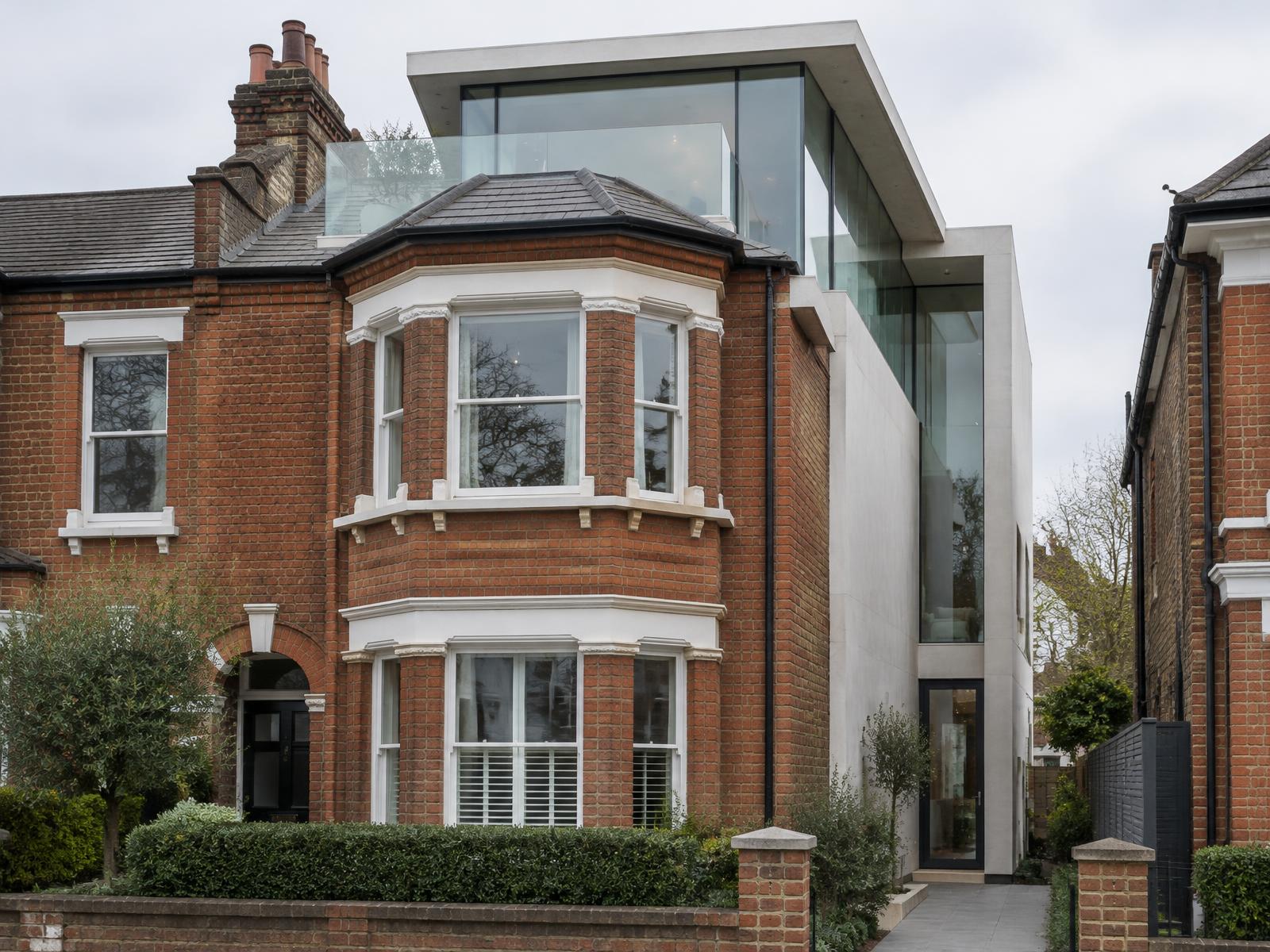Red-brick Victorian bay-fronted terrace house with a contemporary glass and white stone addition rising behind it