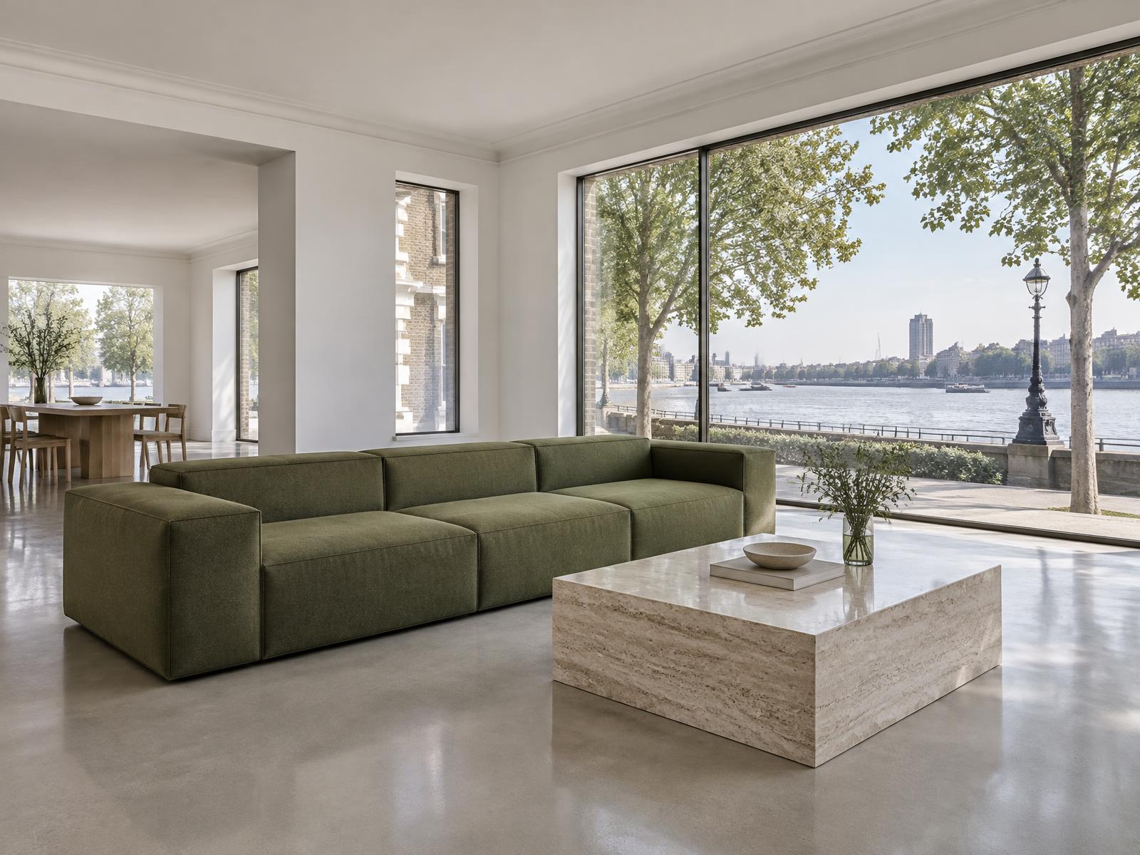 Minimalist room with a square-edged olive sofa and floor-to-ceiling glass onto the Thames riverside