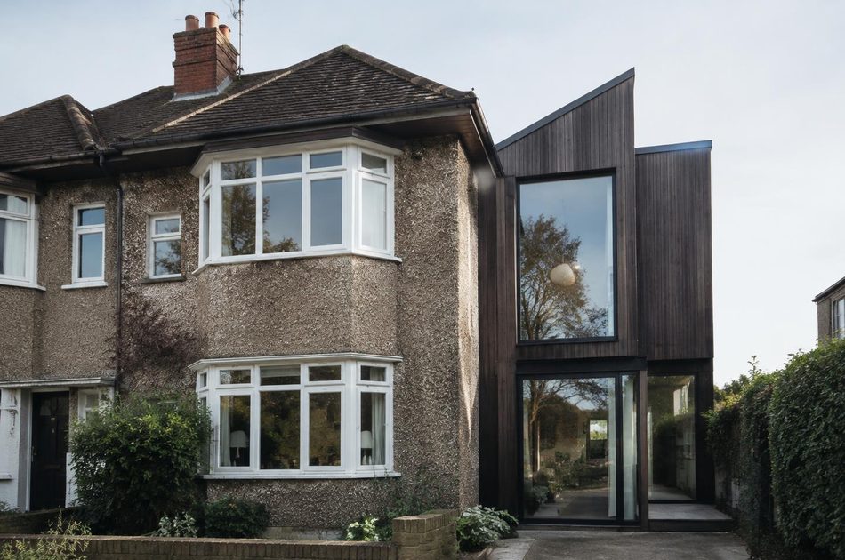 Pebbledashed interwar semi beside a charred timber extension in Greenford