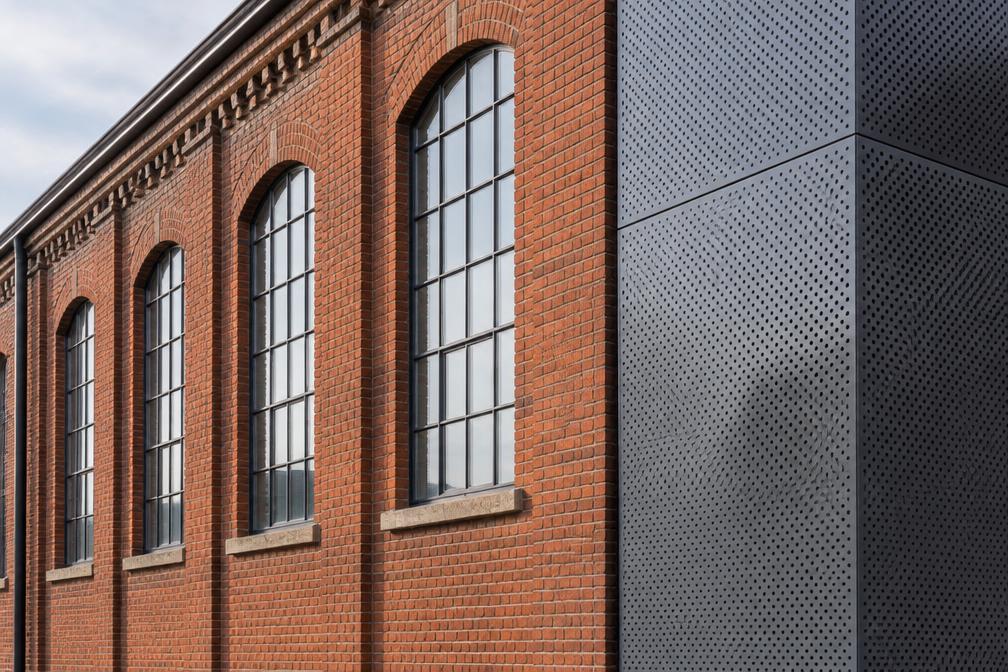 Industrial brick facade beside new perforated metal cladding in Hayes