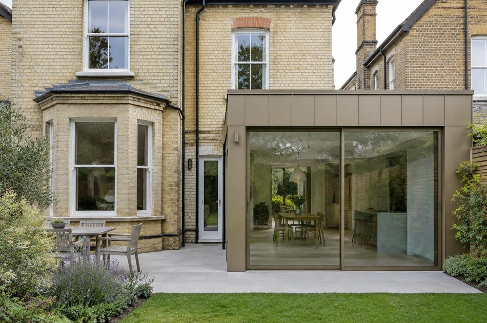Pale brick Victorian house beside a bronze metal and glass extension in Lee