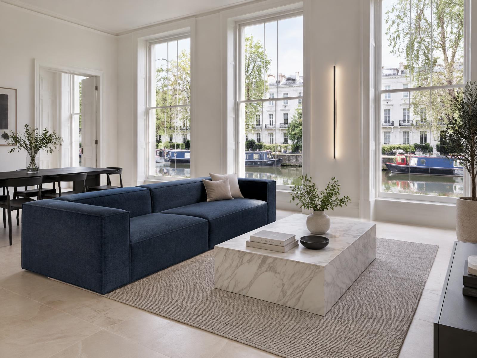 Minimalist mansion-block flat with a square-edged navy sofa and windows onto the canal and stucco villas