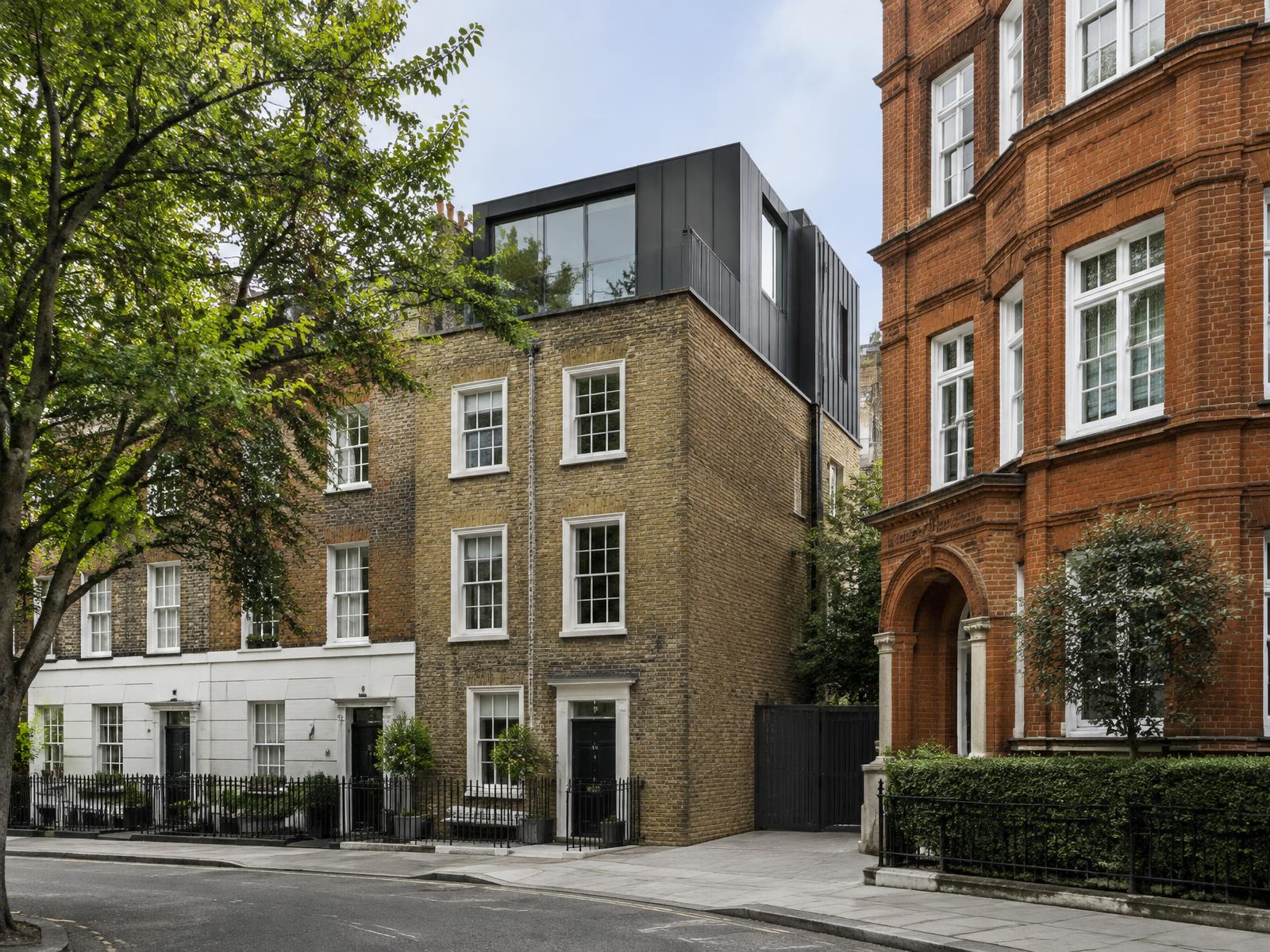 Yellow stock brick Marylebone terrace house with a dark zinc and glass roof addition beside a red-brick Edwardian mansion block