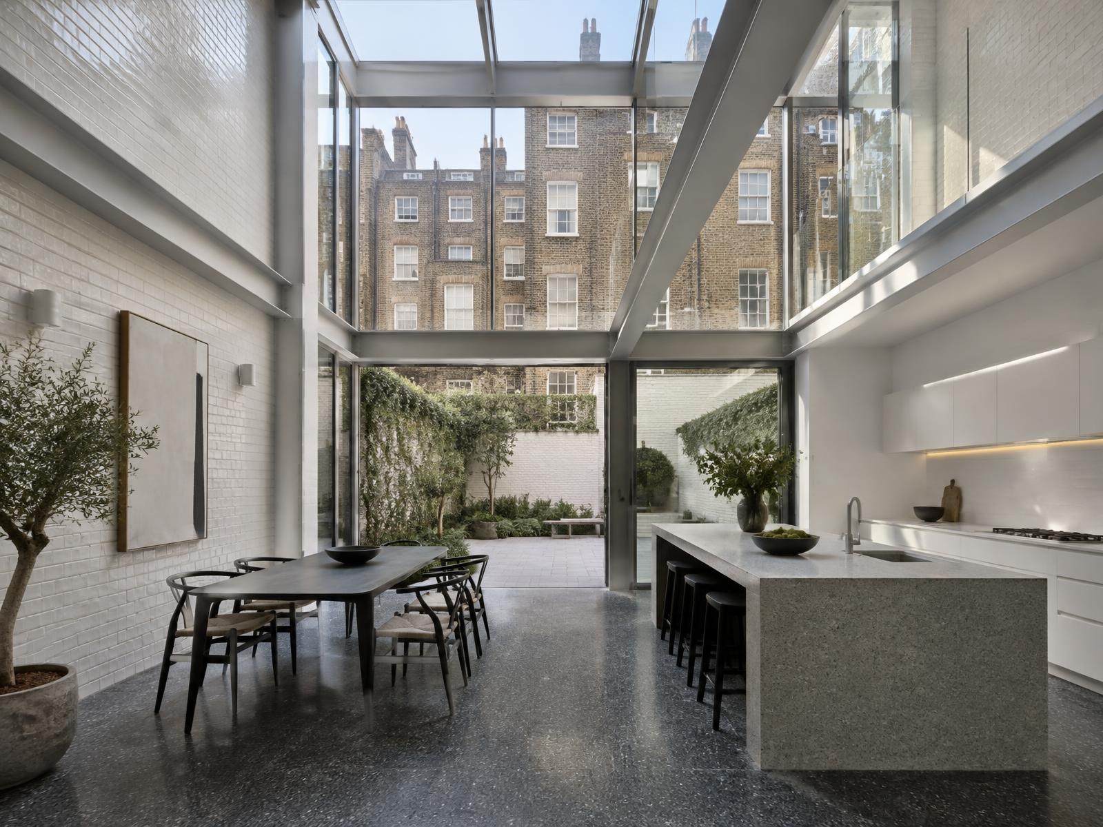 Double-height steel and glass rear wing with granite island, looking onto Georgian brick rear elevations in Mayfair