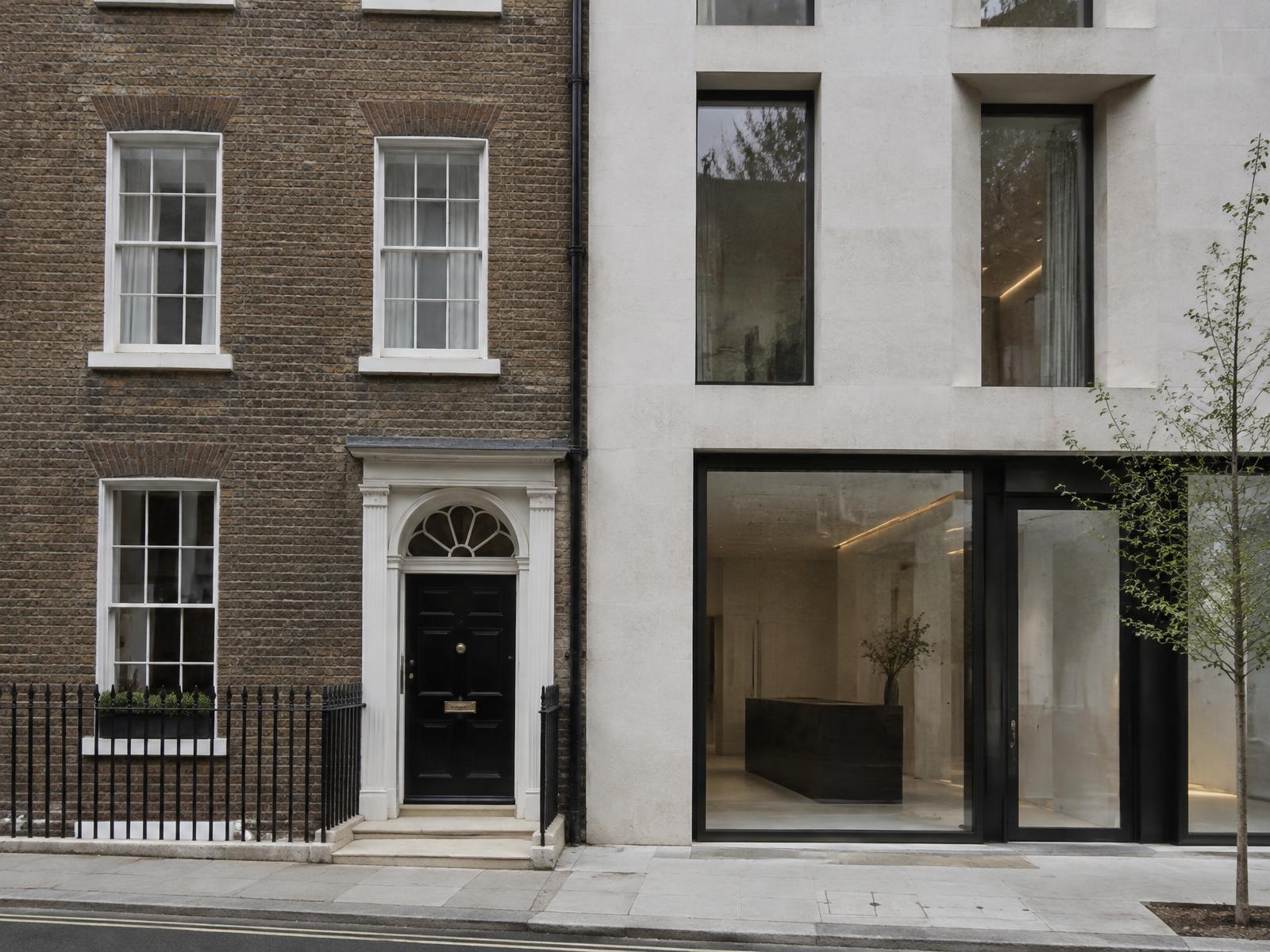Brown-brick Georgian Mayfair townhouse directly beside a contemporary pale limestone building with deep-set glazing