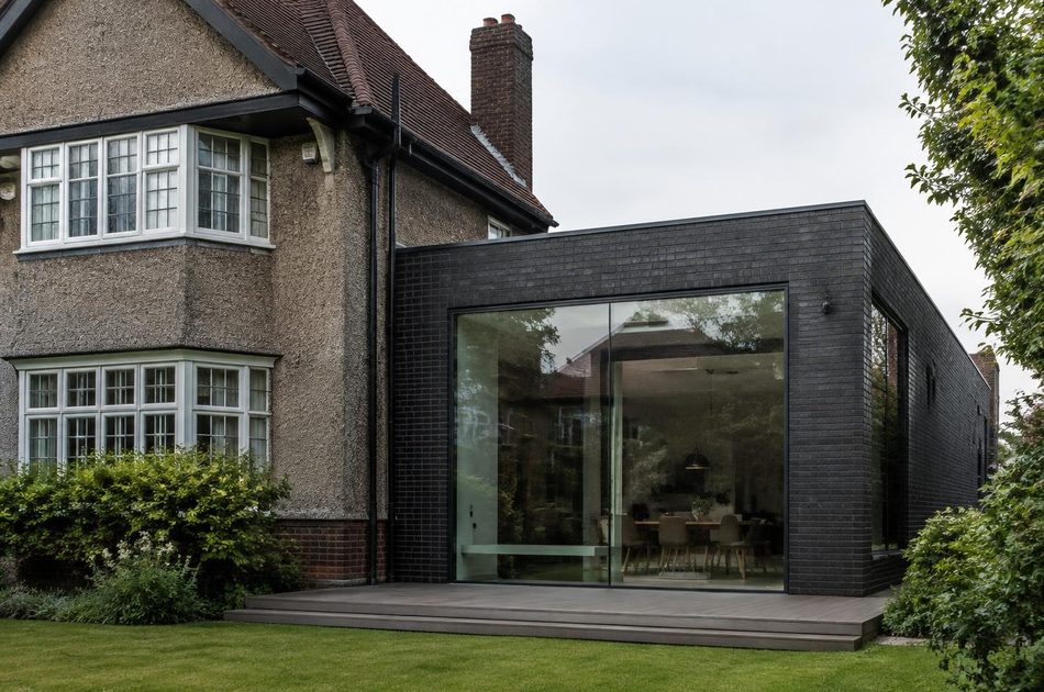 Garden-suburb house beside a dark brick and glass extension in Merton