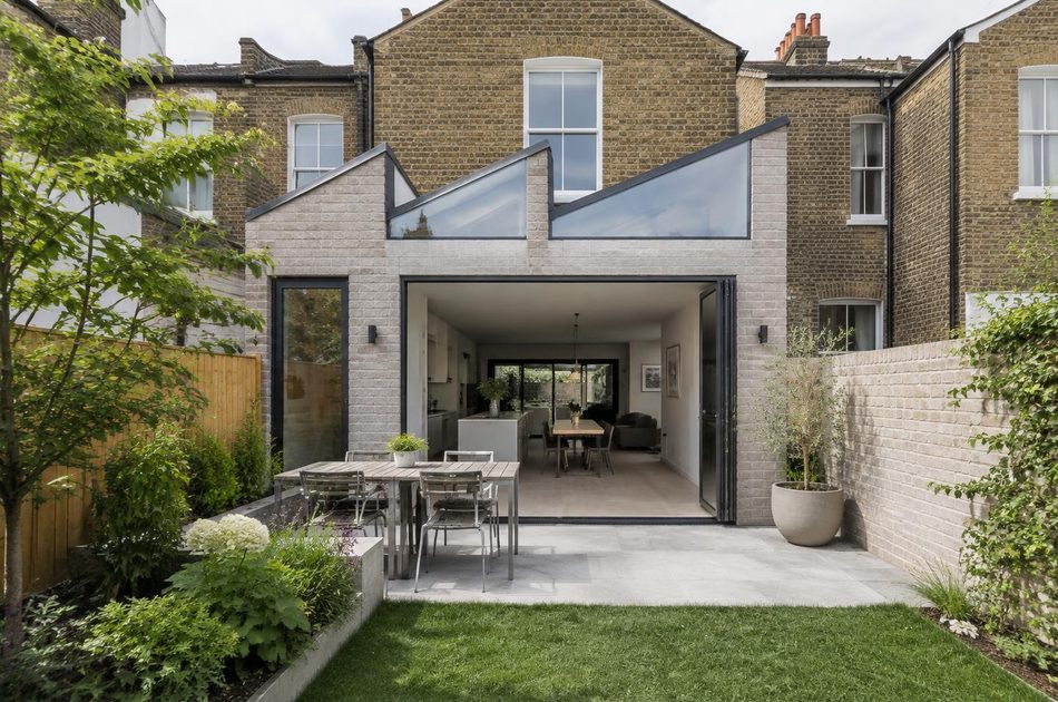 Pale brick sawtooth-roof rear extension behind Victorian terraces in Mitcham