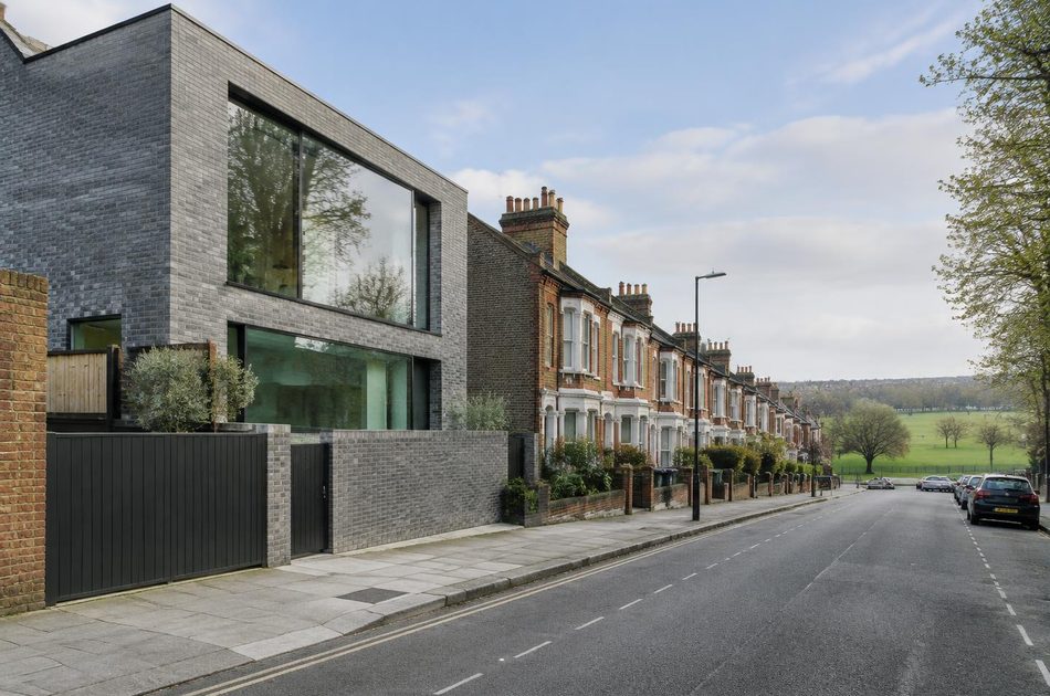 Victorian terraced street towards an open green beside a contemporary grey brick house in Mitcham