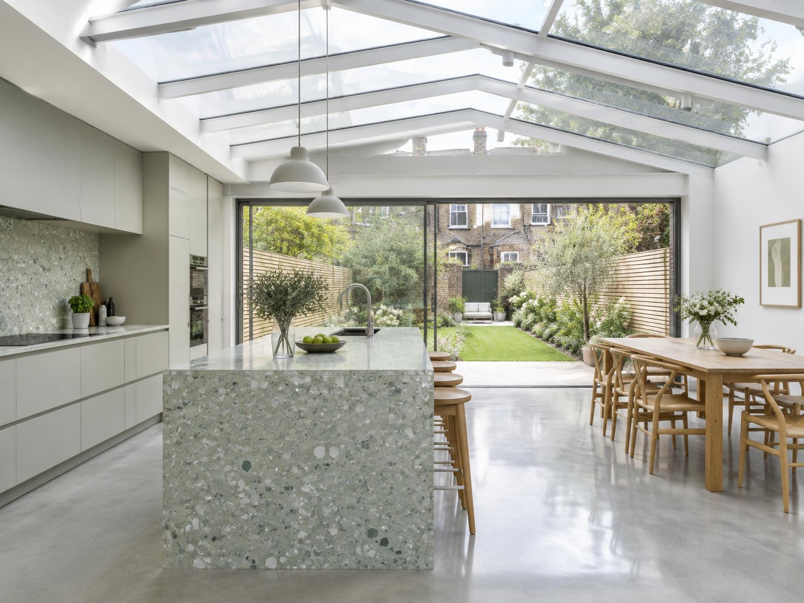 Rear kitchen extension with a glass roof, white steel beams and a pale green terrazzo island