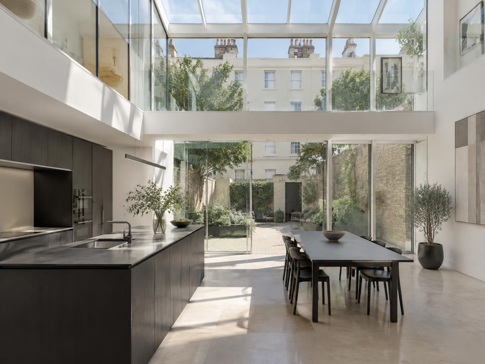 New double-height glazed rear wing with a dark kitchen opening onto a garden behind stucco terraces