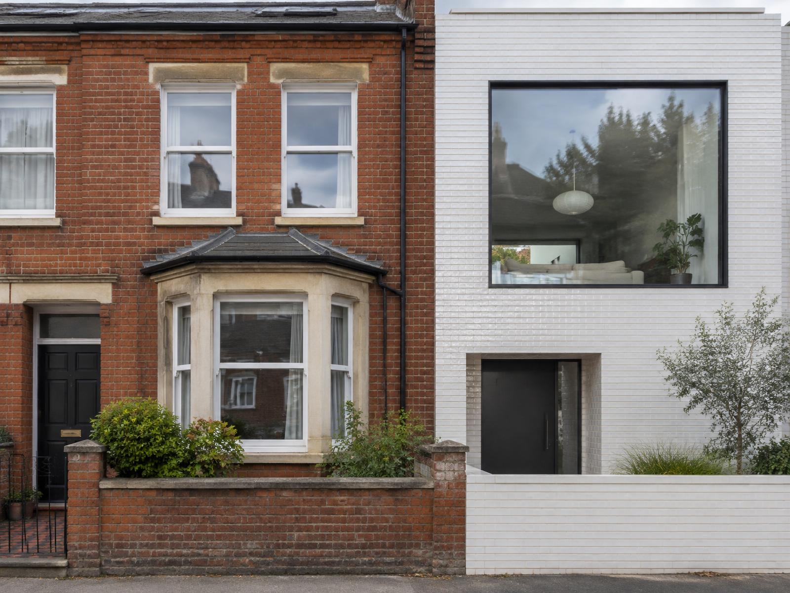Red-brick Victorian terrace house directly beside a contemporary white glazed-brick house with a large square window