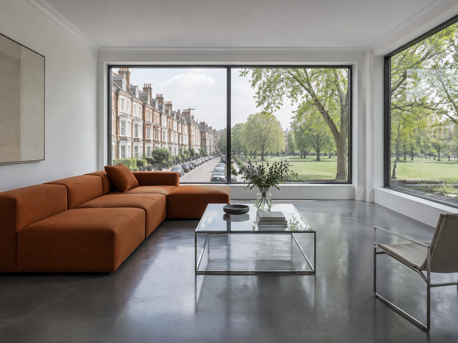 Minimalist room with a square-edged rust sofa and wide windows onto Victorian terraces and a green