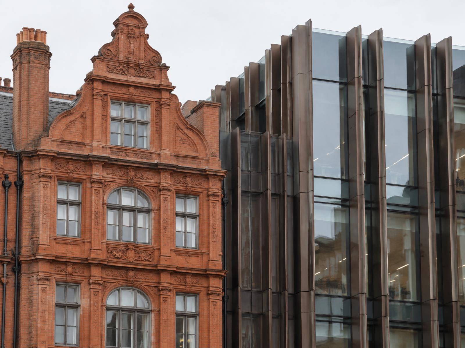 Ornate red brick and terracotta gabled facade directly beside a bronze-finned glass building