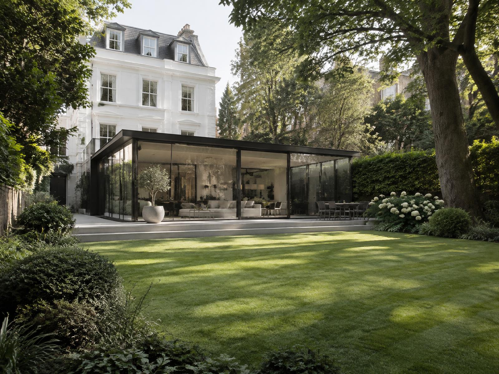 Large leafy garden behind a stucco villa with a contemporary dark-framed glass pavilion extension