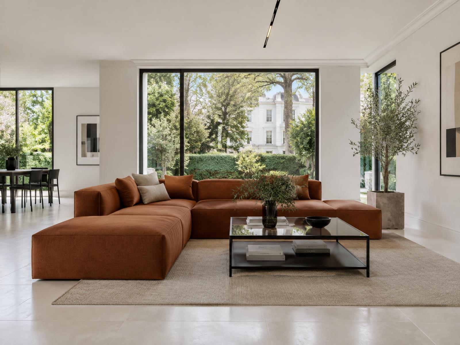Minimalist villa living room with a square-edged rust sofa and large windows onto a leafy garden