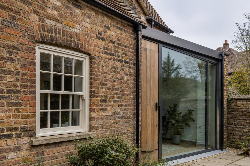 Old brick cottage wall meeting a slim glazed extension in Walthamstow Village