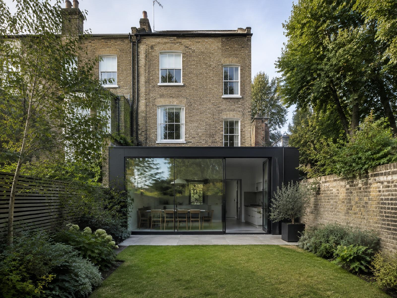 Yellow brick Victorian terrace house with a black glass extension and mature trees beyond