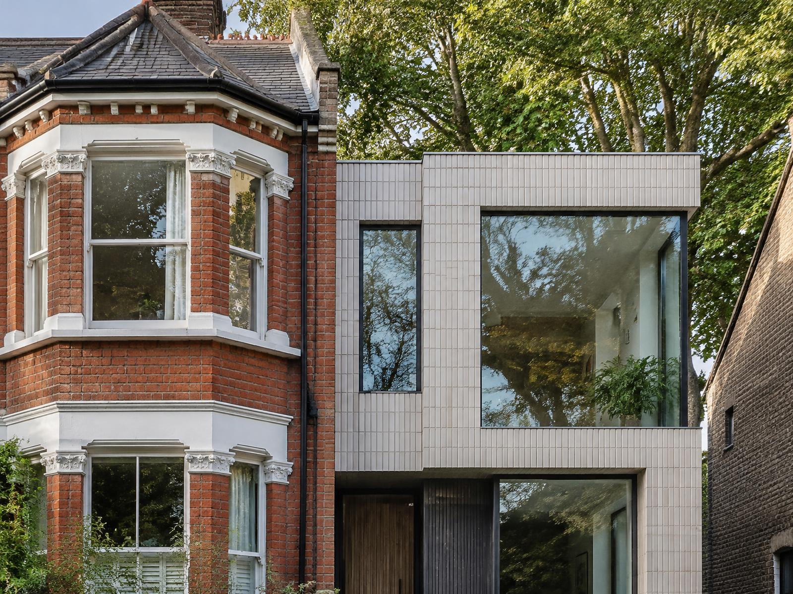 Red brick Victorian bay-fronted house directly beside a pale ceramic-tiled contemporary house with trees behind