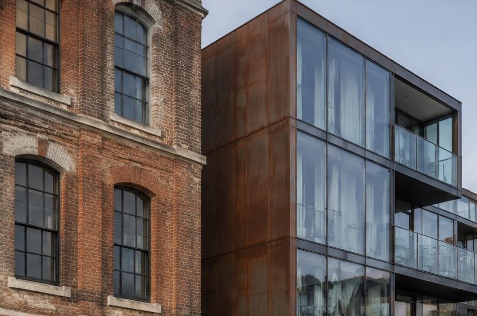 Historic arsenal brick facade beside a weathered-steel and glass extension in Woolwich