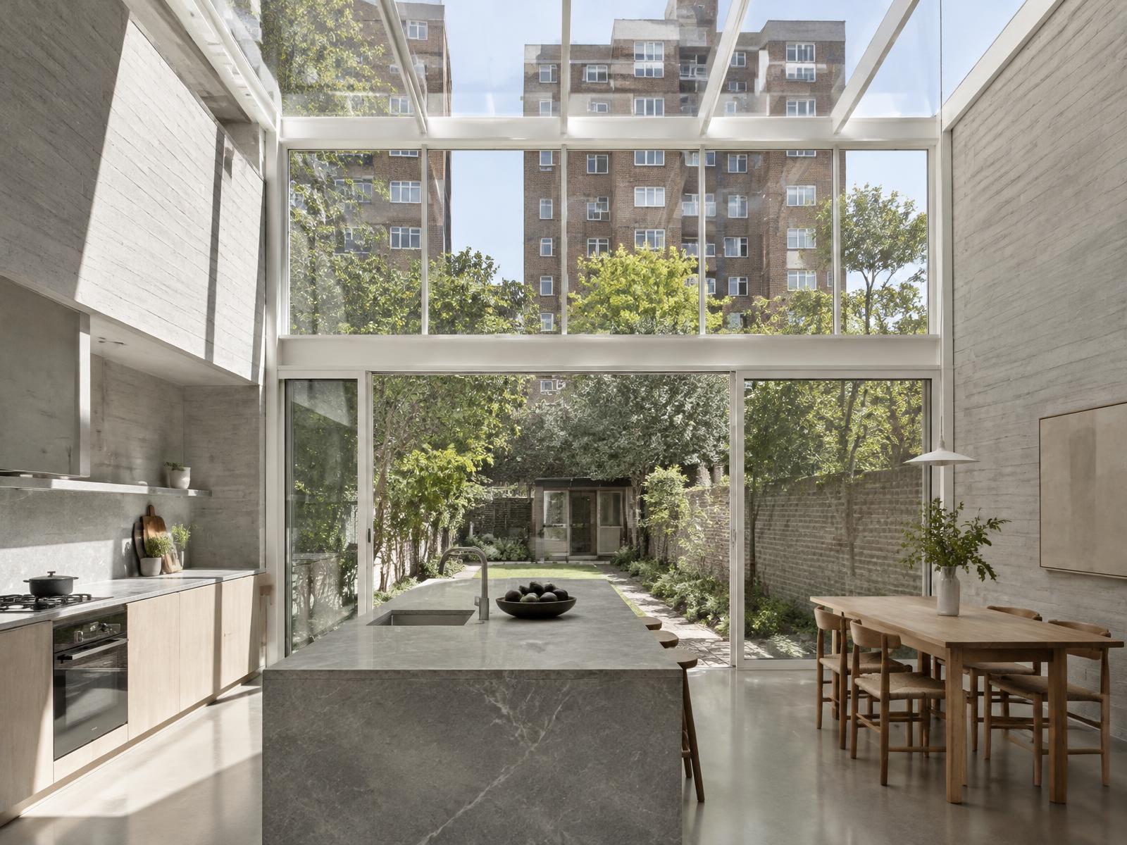 New double-height kitchen with board-marked concrete and a glass roof looking onto a garden and estate towers