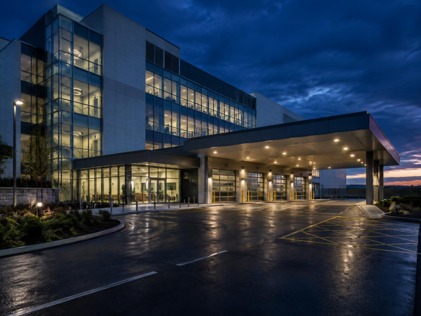 Generic modern healthcare building with glazed entrance and covered ambulance bay forecourt at dusk